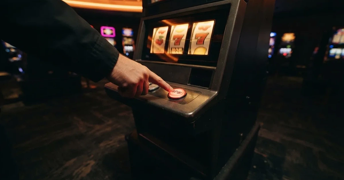 Ett finger trycker på spelautomatens klarröda knapp i dunklet, neonljus lyser runt omkring — 100 free spins casino i sverige