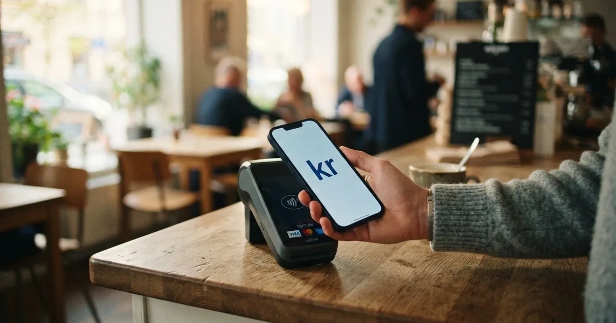 En hand håller ett betalkort nära en kortterminal för en kontaktlös betalning, fotograferat i närbild med varm belysning.